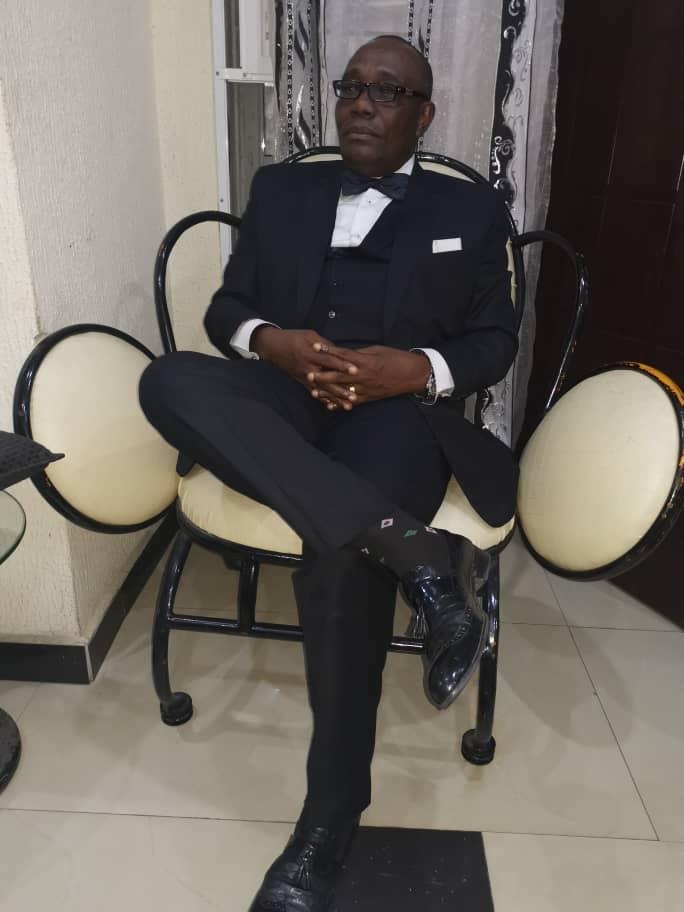 Apostle Prosper seated in formal attire with bowtie