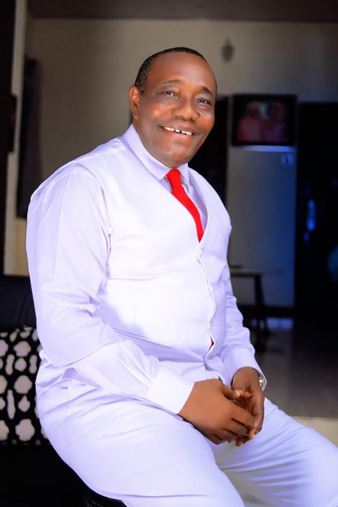 Apostle Prosper Okujere smiling in white suit and red tie
